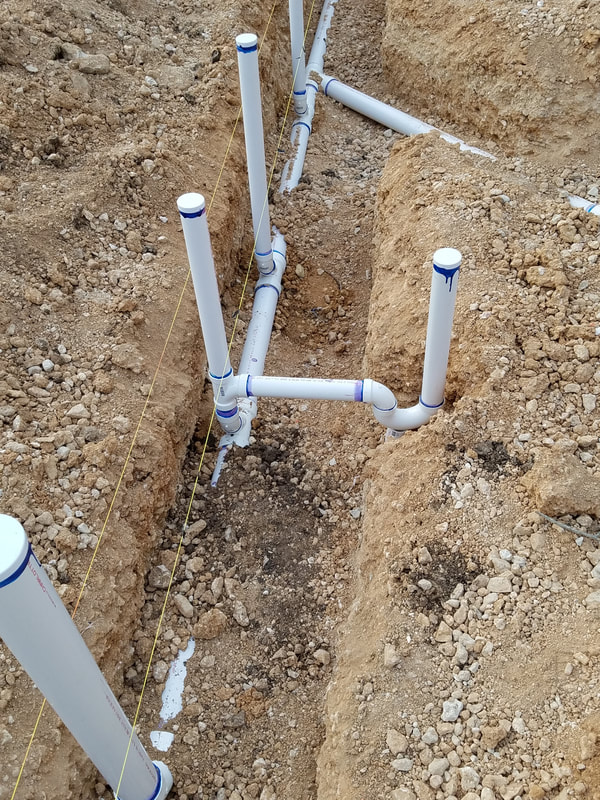 White PVC plumbing pipes are installed in a shallow trench on a construction site, indicating preparation for drainage or irrigation systems.