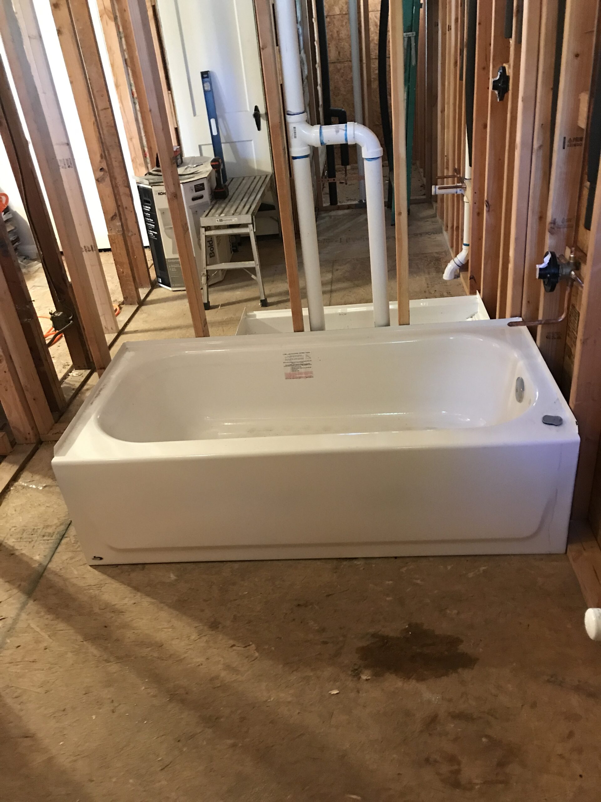 Newly installed bathtub with plumbing in place, surrounded by unfinished walls and construction materials, indicating ongoing home renovation.