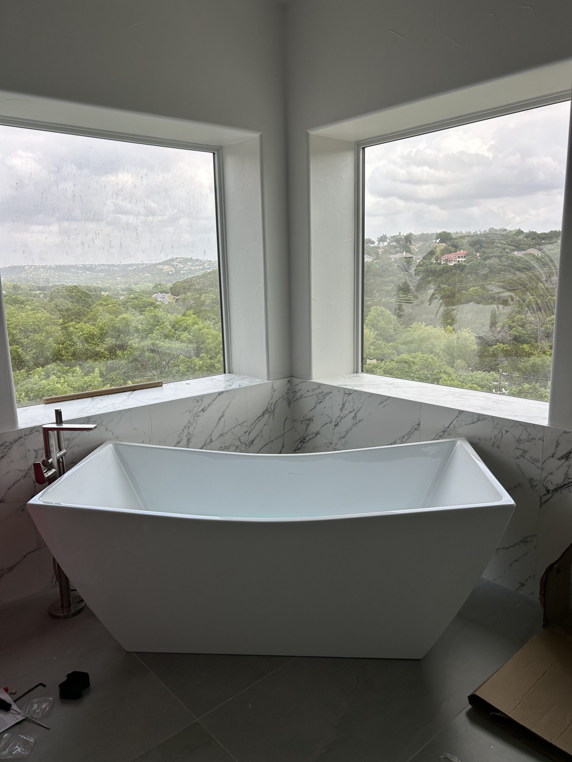 Luxury freestanding bathtub in a marble bathroom corner with large scenic windows, completed by our plumbing service in Georgetown, TX. Contact us today to upgrade your bathroom.