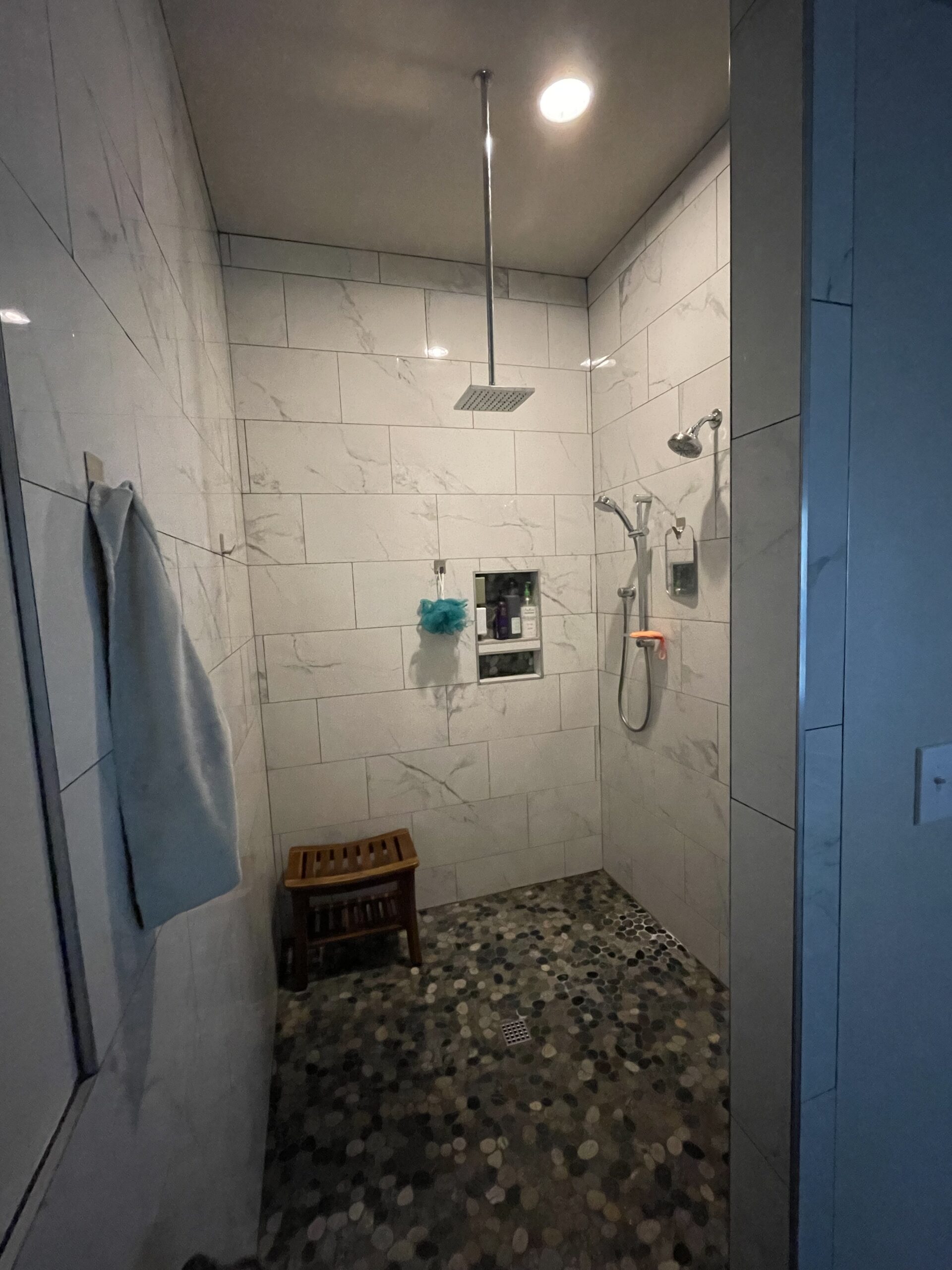 Modern shower space featuring marble walls, a rainfall showerhead, and a wooden stool. The design emphasizes cleanliness and relaxation.