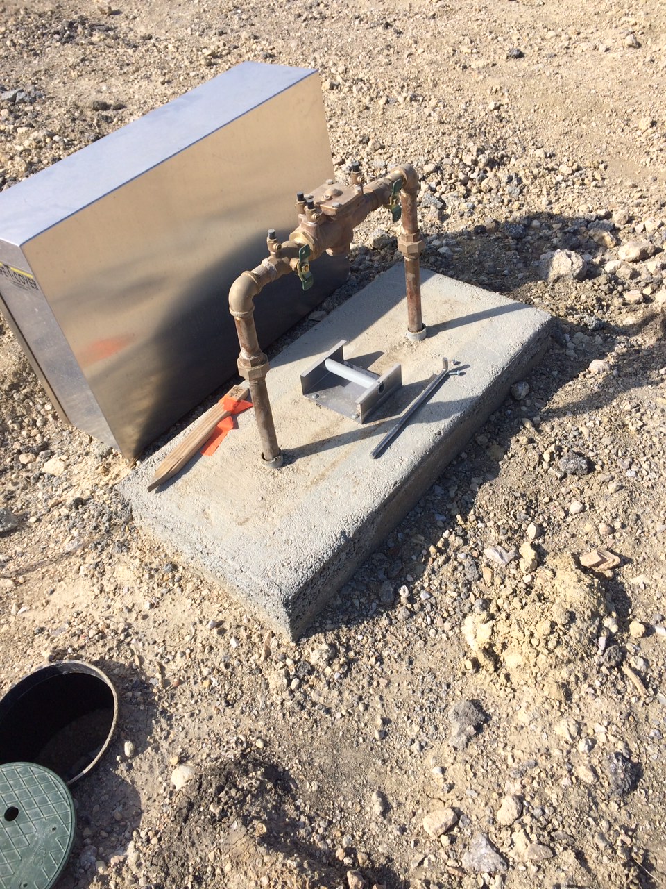 Newly installed water meter with pipes and tools on a gravel surface, indicating ongoing construction or utility work.