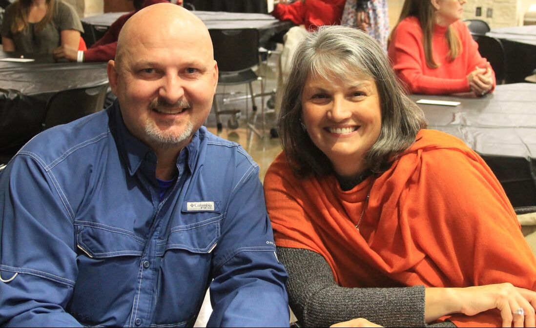 A man and a woman smile while sitting together at a gathering, highlighting a moment of camaraderie at the event.